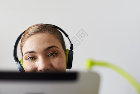 使用绿色耳听器收听在电脑板块上的播音音乐的妇女图片