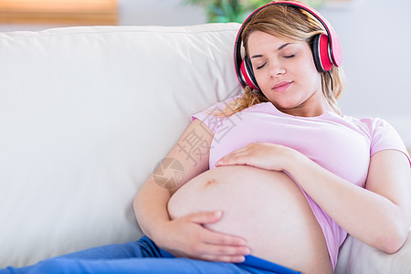 孕妇倾听音乐和抚摸肚子的女孕妇女士客厅睡眠成人母亲说谎长椅听力公寓分娩图片
