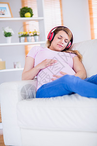 孕妇倾听音乐和抚摸肚子的女孕妇耳机沙发腹部家庭生活听力孕妇装成人长椅育儿家长图片