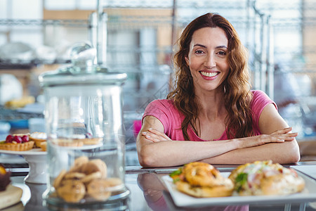 漂亮的黑发美女在柜台后面的相机上微笑咖啡屋糕点餐厅顾客咖啡店女性食堂咖啡馆食品展示图片