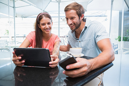 看着笔记本电脑的年轻幸福情侣夫妻男人触摸屏热饮餐厅混血微笑闲暇电话平板图片