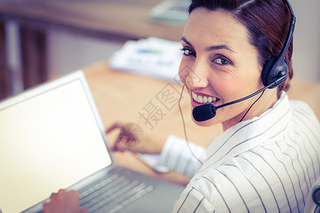 利用笔记本电脑和耳机微笑的棕发白脸色商业妇女桌子公司女士窗户套装女性职业快乐办公室职场图片