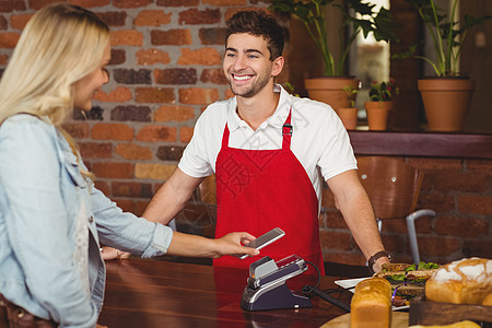 做移动付款的漂亮顾客男人服务器面包咖啡屋工作女性职员支付围裙店铺图片