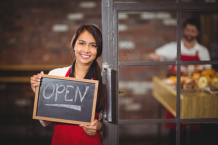 微笑的女服务员展示有开放标志的黑板咖啡师饮料制服行业在职员工男人女性咖啡馆食品图片