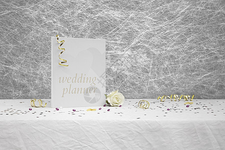 白桌布上的婚礼花板本和金丝带白色策划师黄玫瑰结婚日纸屑丝带白布金子婚书灰色图片