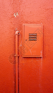 橙色墙上的垂直金属管和电箱;图片