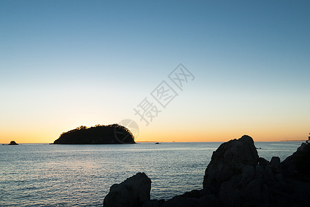 日出时的月光闪烁着天空 环绕着岩石海岸和岸外岛图片