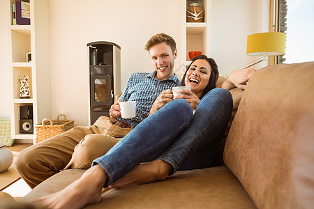 快乐的年轻夫妇在沙发上放松房子女士女朋友棕色热饮男人咖啡服装住所长椅图片