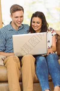 用笔记本电脑在沙发上放松的年轻可爱夫妇休闲房子女性男性闲暇夫妻感情衬衫快乐微笑图片