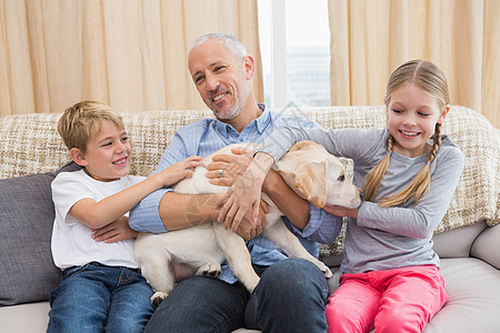 父亲和孩子一起坐在沙发上跟小狗玩高清图片