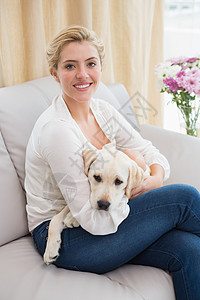 快乐的金发金发美女和沙发上的小狗抱在一起拥抱女士家庭生活闲暇公寓微笑女性长椅宠物服装图片