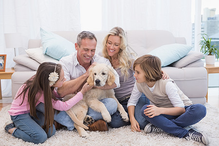 在地毯上带着宠爱的黄拉布拉多 微笑的家庭小狗孩子长椅快乐女孩客厅男性父亲女性家庭生活图片