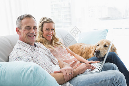 一对夫妇用笔记本电脑 和他们的狗一起花时间家畜客厅女性闲暇男人男性家庭服装宠物公寓图片