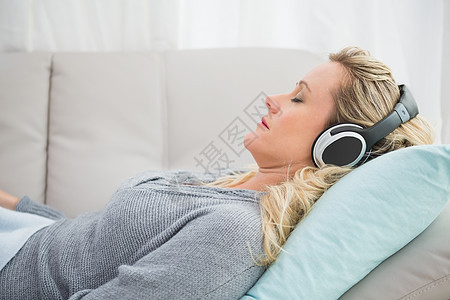 快乐的女孩听音乐 躺在沙发上长椅客厅公寓家庭生活女性休闲耳机家庭房子微笑图片