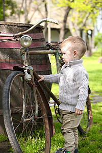 2岁好奇的婴儿男孩 绕着旧自行车走来走去运输小男孩童年孩子羊毛男人男性毛衣村庄踏板图片