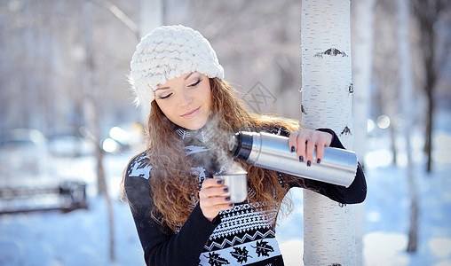美丽的黑发美女在冬天散步时 从热水中倒咖啡图片