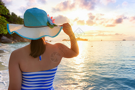 日出时在海滩上的女孩泳装游客日落热带天空帽子闲暇旅行女士海洋图片