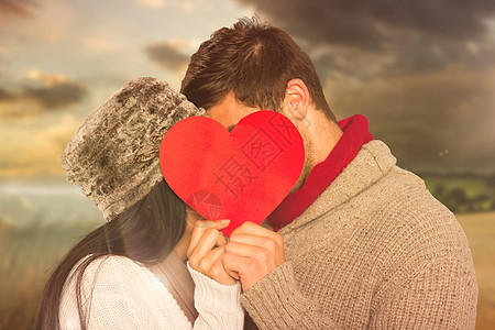 年轻情侣在红心后亲吻的复合形象快乐地平线森林拥抱日落衣物天空亲密感男朋友女士图片