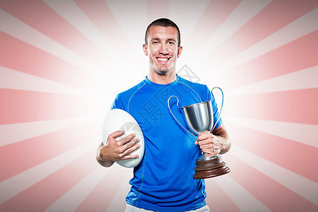拥有奖杯和球的微笑橄榄球运动员画像综合图象竞赛裁剪红色白色反射蓝色胜利金属男性运动图片