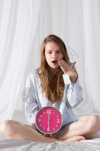 女孩坐在床上 大粉色钟表 上午6时女士小时衬衫金发长发女性就寝成人福利卧室图片
