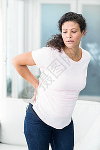 背部疼痛的妇女站在沙发旁图片