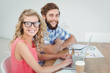 在办公桌上使用笔记本电脑的微笑男人和女人的肖像图片