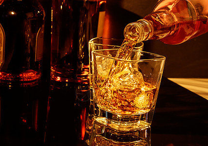 在威士忌玻璃和瓶子前倒威士忌的酒客图片