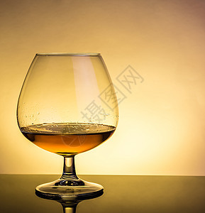 以优雅的典型白兰地玻璃杯中的白兰地喷口水 放在有反光面的桌上图片