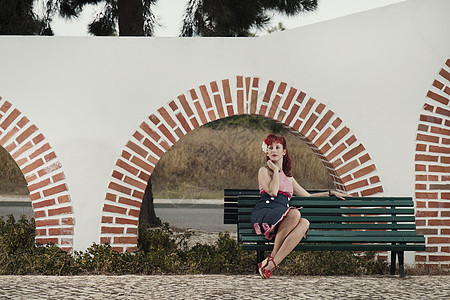 身着旧式服装的年轻女子城市女性发型魅力头发木头红色长椅裙子公园图片
