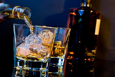 酒巴手倒在两杯威士忌里 桌上有冰块 桌子上装有轻色蓝色和反光瓶子乡村饮料餐厅酒精立方体琥珀色酒保反射液体图片