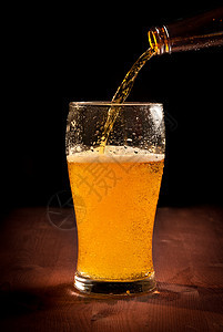 从瓶中倒入玻璃的新鲜啤酒流动木头瓶子液体庆典酒吧飞沫酿造金子餐巾图片