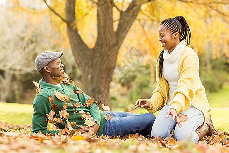 看见一对年轻微笑的夫妇在树叶上保暖衣服夫妻享受衣物环境活动乐趣绿地草地图片