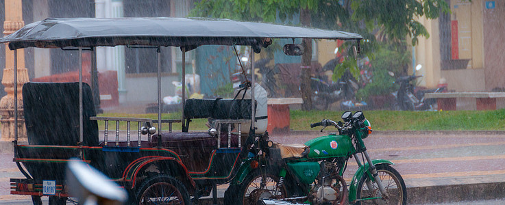 Tuktuk 在贡布的雨季风中进行自动循环摩托车运输出租车街道下雨人力车天气摩托图片