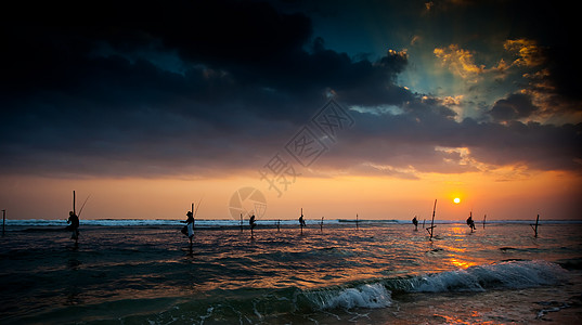 日落之夜传统矮渔夫的休眠轮椅平衡男人日落鱼人海洋海岸高跷海浪天空男性图片