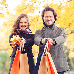 带有购物袋的夫妇叶子夫妻公园喜悦微笑购物男人女士黄色展示背景图片