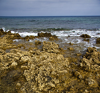 在兰萨罗特岛的 白叶泡沫石头云层沙滩中的水图片
