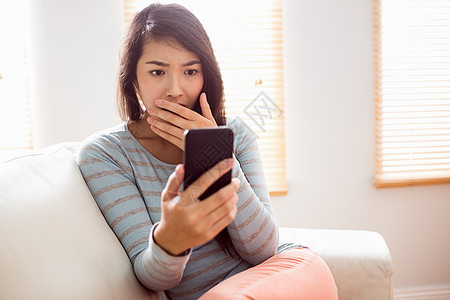 亚裔女性阅读令人震惊的文字房子技术休闲住所客厅手机电话闲暇短信震惊图片