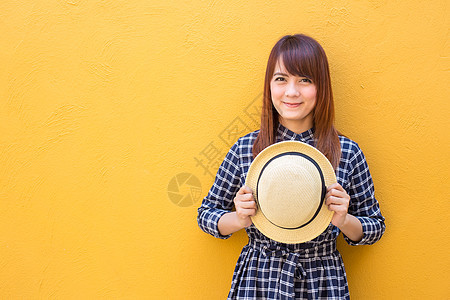 带着黄色水泥墙的帽子 穿着着衣服戴着笑着微笑的妇女喜悦女性白色裙子享受服装女士快乐成人乐趣图片