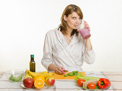 坐在厨房桌边的年轻女孩 喝着一个大杯子上的水果奶昔图片