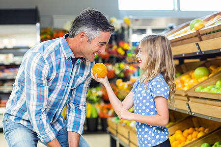 可爱的女孩拿着橙子给爸爸看产品水果男人顾客杂货店橙子微笑服装架子零售图片