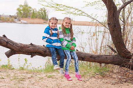 两个女孩坐在河岸的一棵落树上图片