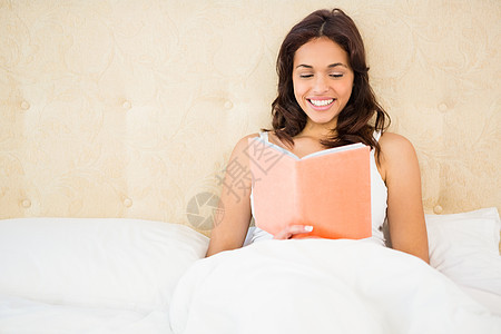 漂亮女人在床上看书公寓卧室混血闲暇房子阅读枕头女性坐垫微笑图片