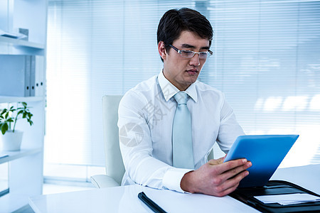 严重的亚洲商务人士使用他的平板电脑男生药片领带套装滚动旋转椅眼镜男性办公室职业图片