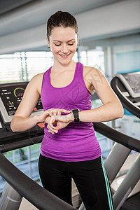 在跑步机上使用智能手表的微笑健美的女人跑步训练身体技术女性健身计算活动调子移动图片