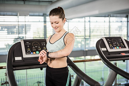 使用智能手表在跑步机上微笑的女人计算运动健身房运动服调子力量跑步设备电脑俱乐部图片