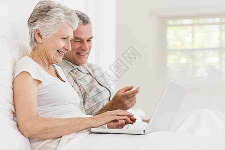 在床上使用膝上型电脑的老年夫妇羽绒被讨论女性棉被卧室闲暇房子枕头男性微笑图片