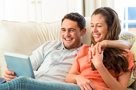 年轻夫妇在沙发上使用数字平板电脑时玩得开心图片