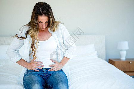妇女坐在床上 忍着肚子的肚子图片
