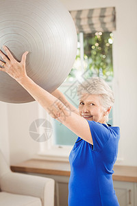 高级女性在锻炼时举起球头发力量健身健身房女士沙发休闲运动公寓拉伸背景图片