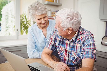 使用笔记本电脑时同年长夫妇谈话男性老年人专注男人住所家庭倾斜厨房服装技术图片